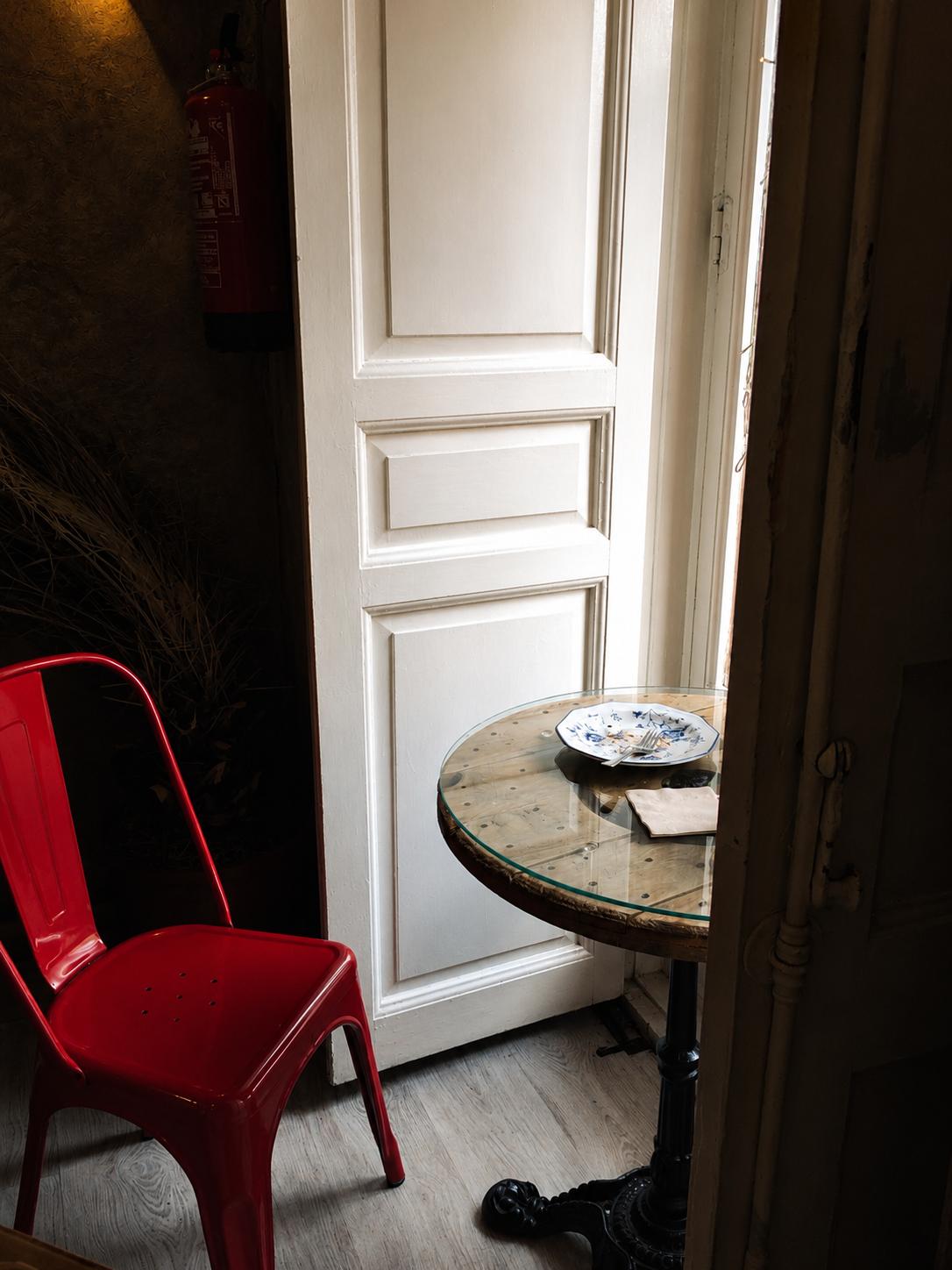 Una puerta entreabierta junto a una mesa y una silla roja